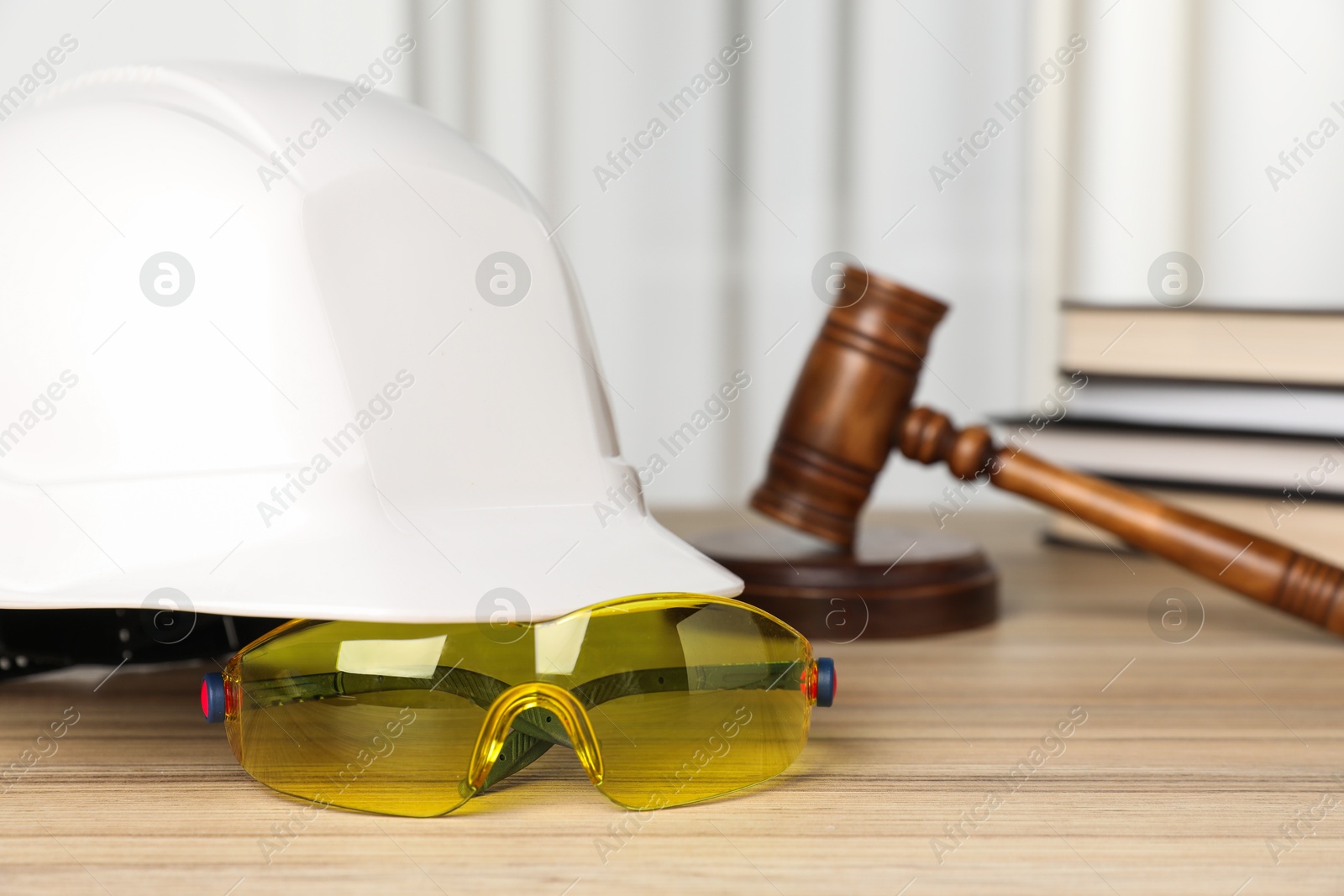 Photo of Accident at work. Goggles, hardhat and gavel on wooden table, selective focus