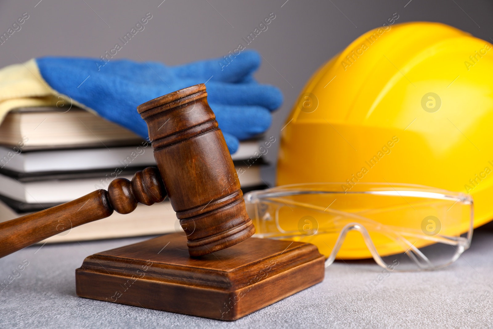 Photo of Accident at work. Gavel, safety equipment and stack of books on grey textured table, selective focus