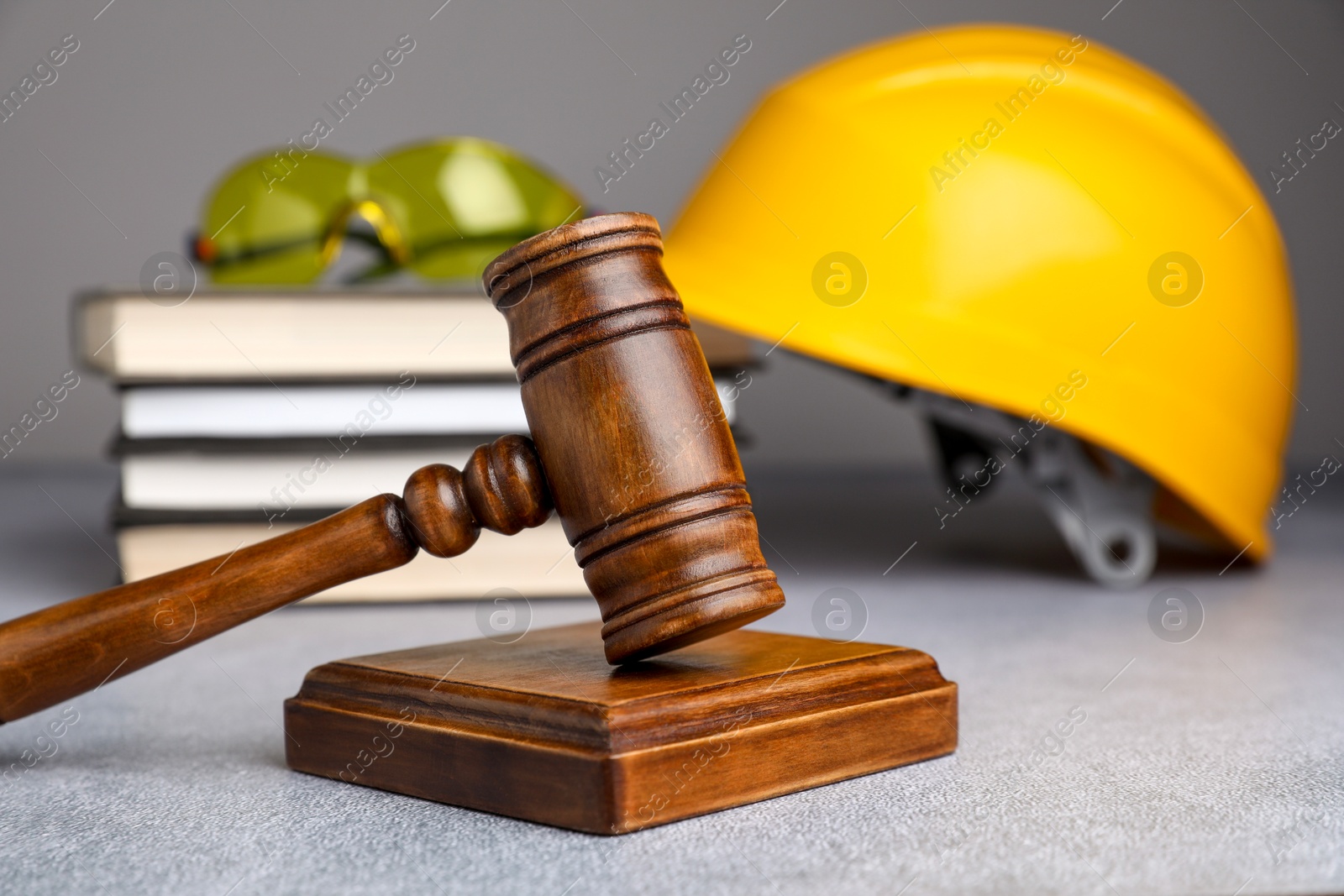 Photo of Accident at work. Gavel, safety equipment and stack of books on grey textured table, selective focus