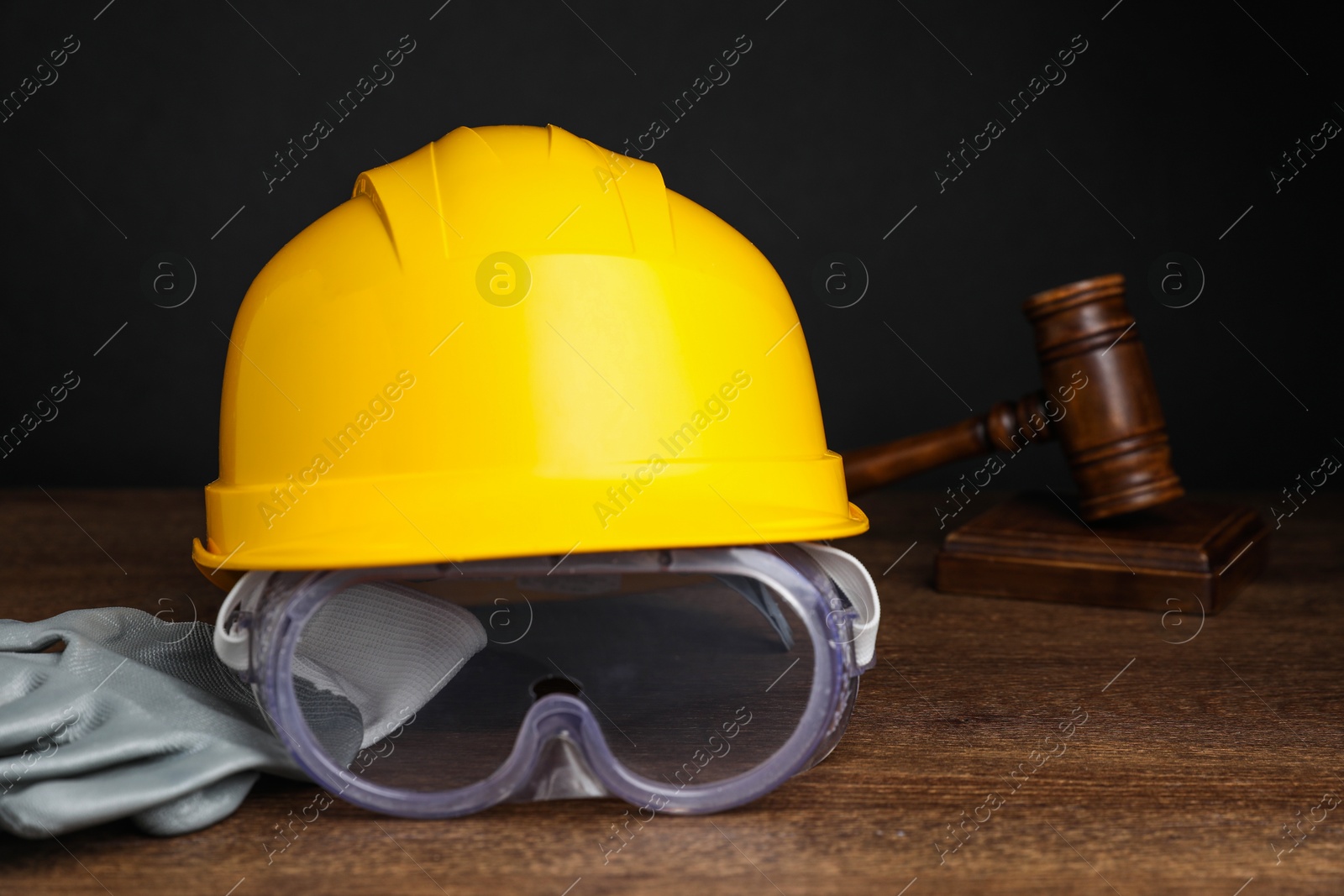 Photo of Accident at work. Hardhat, goggles, gloves and gavel on wooden table, closeup