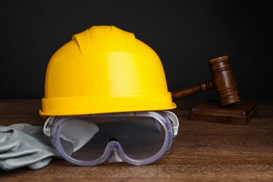 Photo of Accident at work. Hardhat, goggles, gloves and gavel on wooden table, closeup