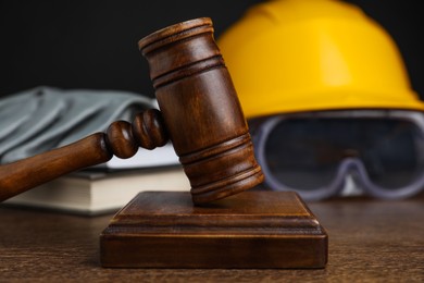 Photo of Accident at work. Gavel, safety equipment and books on wooden table, selective focus