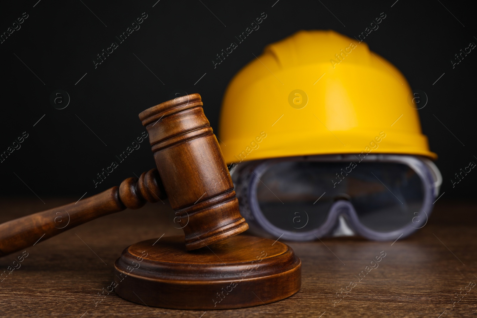 Photo of Accident at work. Gavel, hardhat and goggles on wooden table, selective focus