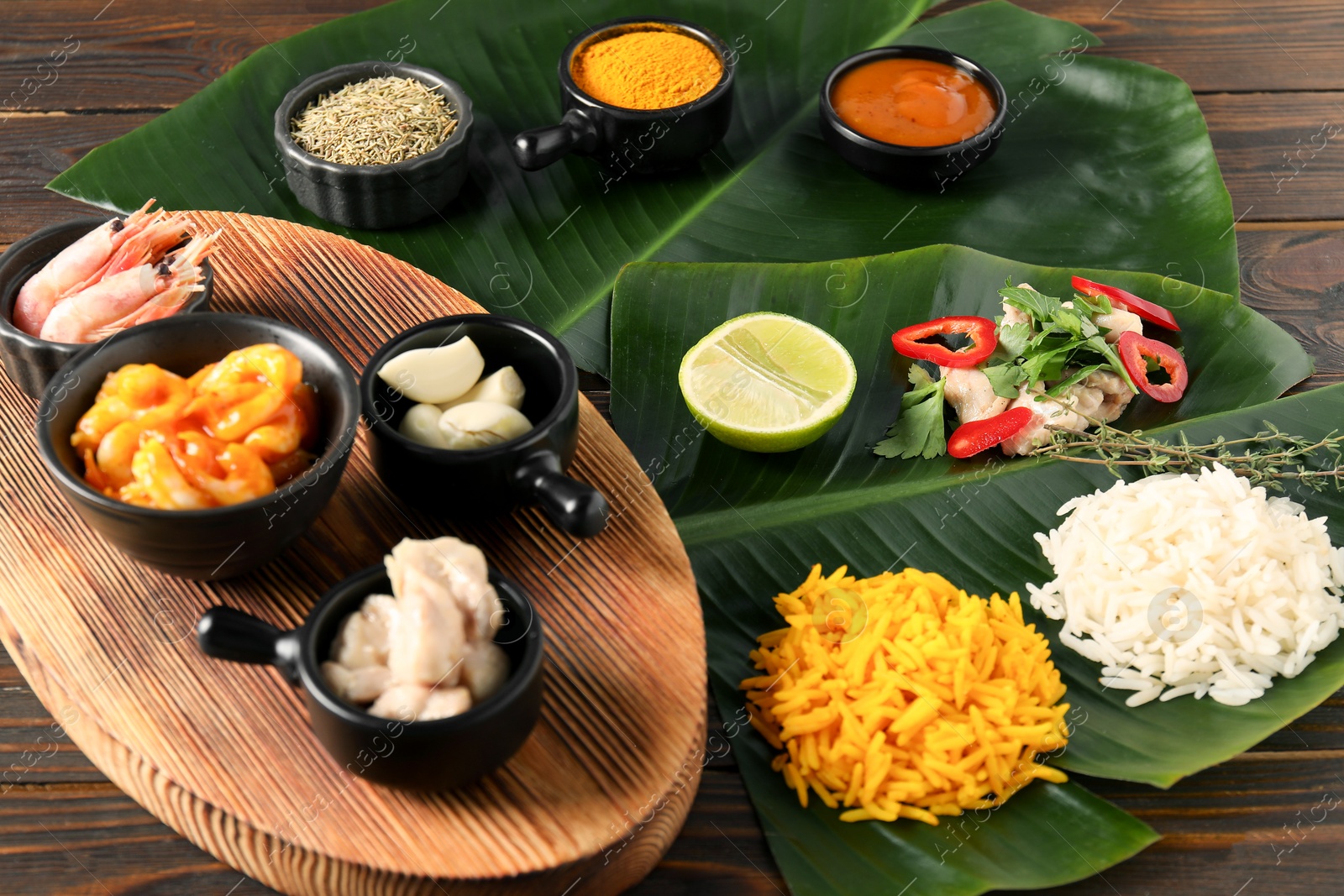 Photo of Cut banana leaves with different food, board, spices and sauce on wooden table, closeup