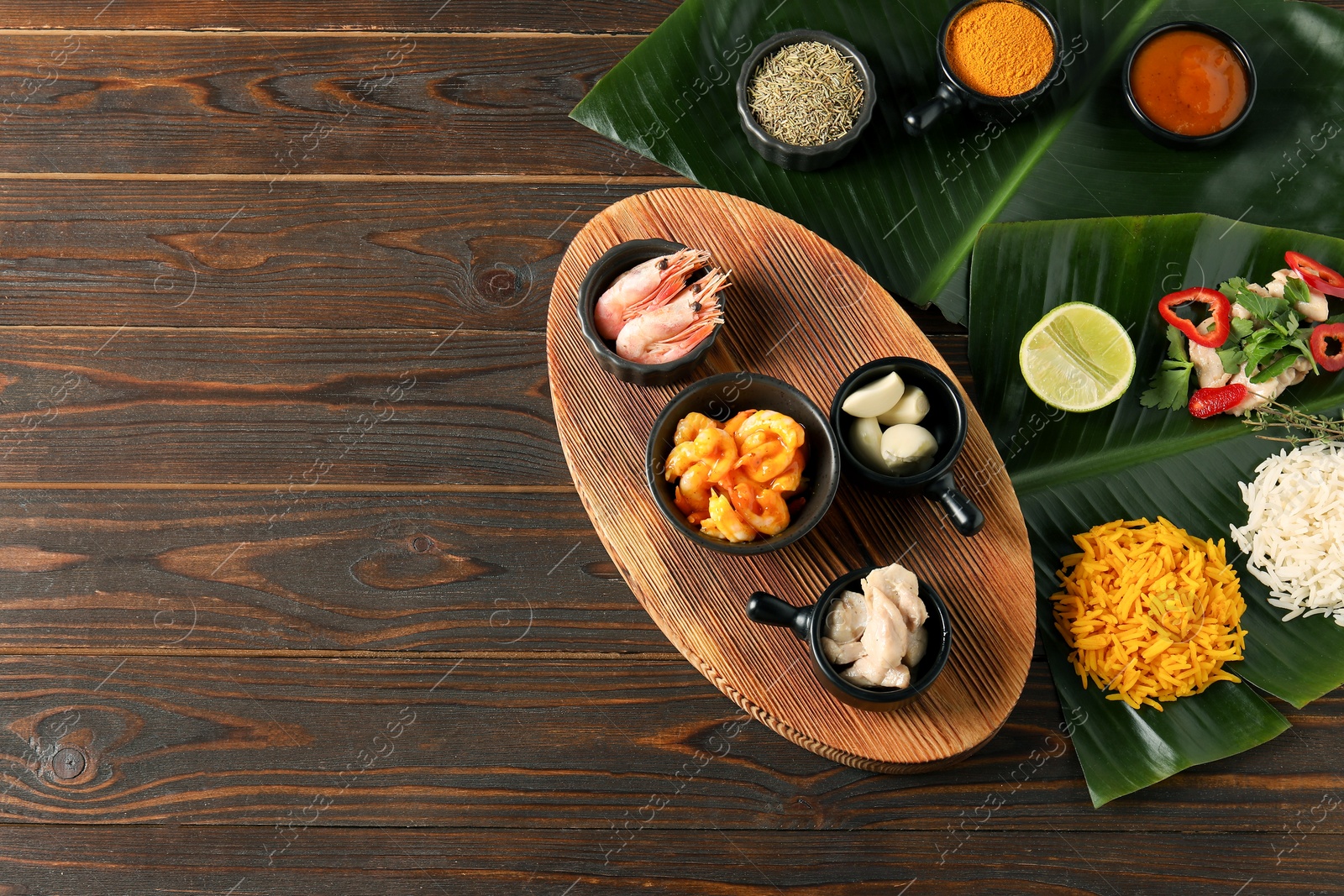 Photo of Cut banana leaves with different food, board, spices and sauce on wooden table, flat lay. Space for text