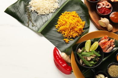 Photo of Cut banana leaves with different food, spices and sauce on white table, flat lay