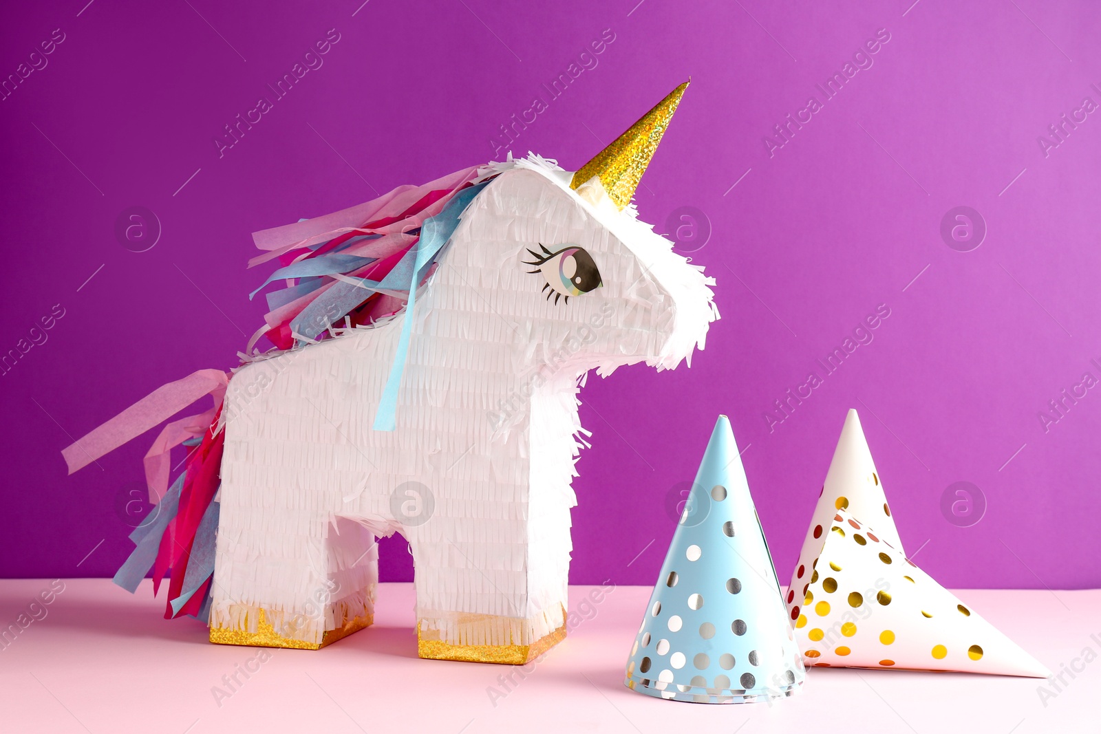 Photo of Bright pinata in shape of unicorn and party cones on color background