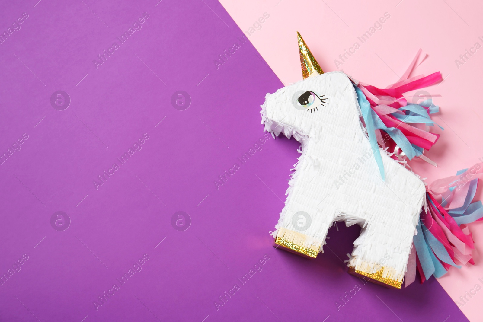 Photo of Bright pinata in shape of unicorn on color background, top view. Space for text