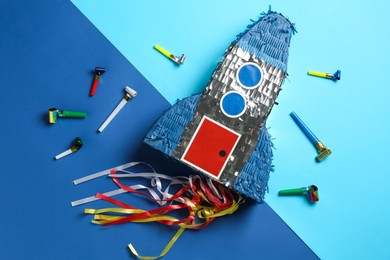 Photo of Bright pinata in shape of spaceship and blowers on blue background, flat lay