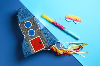 Photo of Bright pinata in shape of spaceship , blindfold and stick on blue background, flat lay