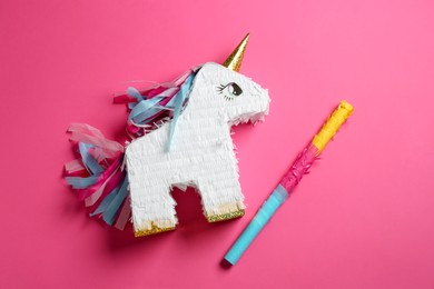 Photo of Bright pinata in shape of unicorn and stick on pink background, top view