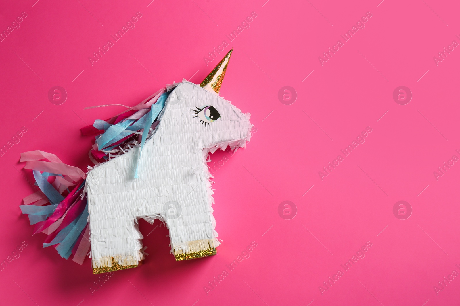 Photo of Bright pinata in shape of unicorn on pink background, top view. Space for text