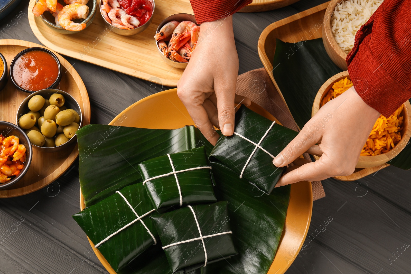 Photo of Woman taking folded banana leaf with food at wooden table with products and sauce, above view