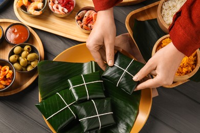 Photo of Woman taking folded banana leaf with food at wooden table with products and sauce, above view