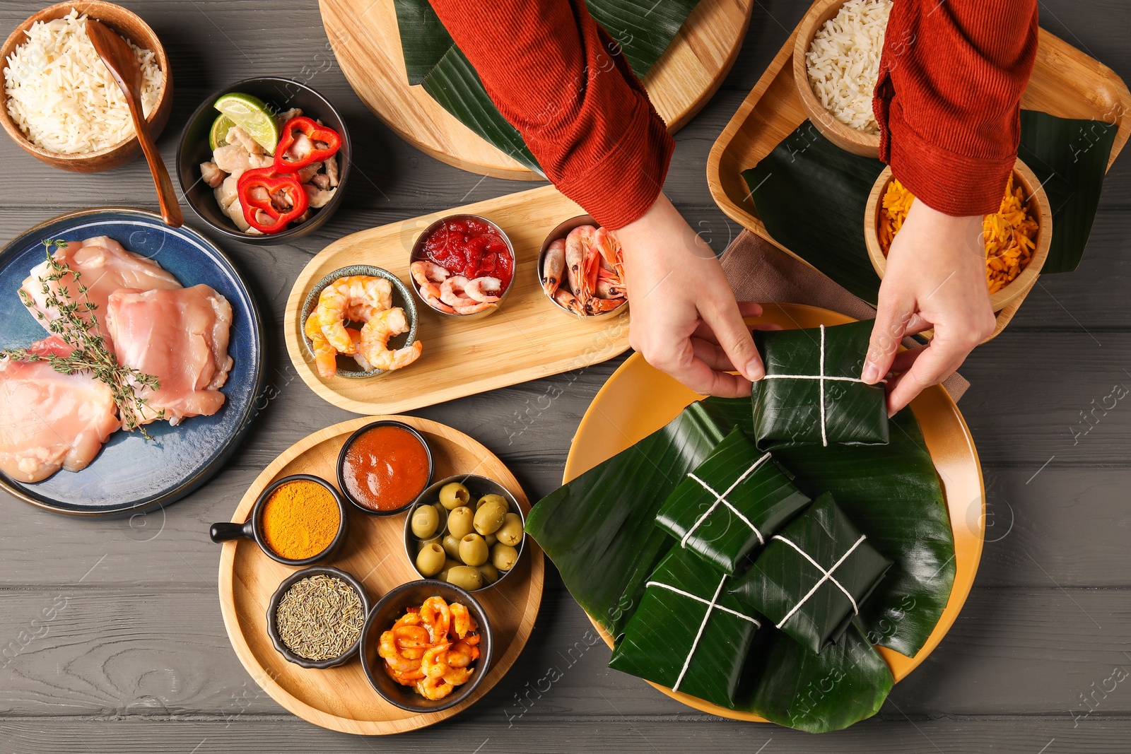 Photo of Woman taking folded banana leaf with food at wooden table with products, top view