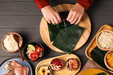 Photo of Woman tying banana leaf with food at wooden table with products, top view. Healthy eco serving