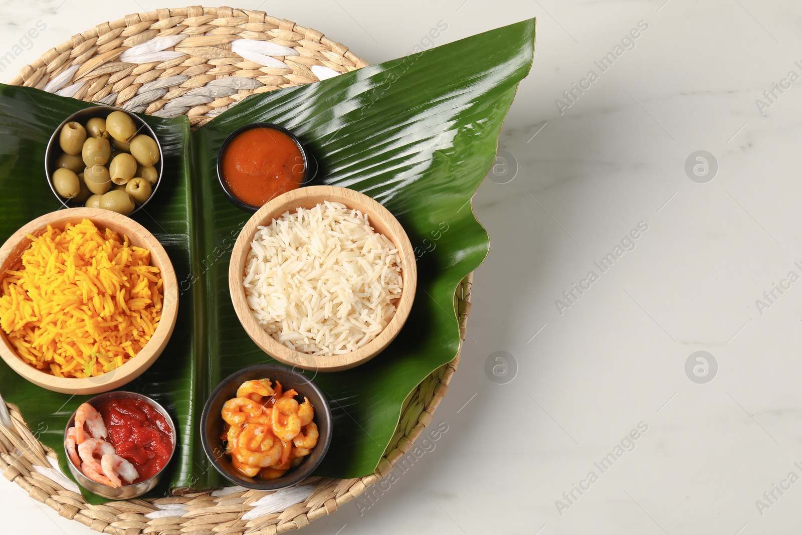 Photo of Piece of banana leaf with different food and sauce on white table, top view. Space for text