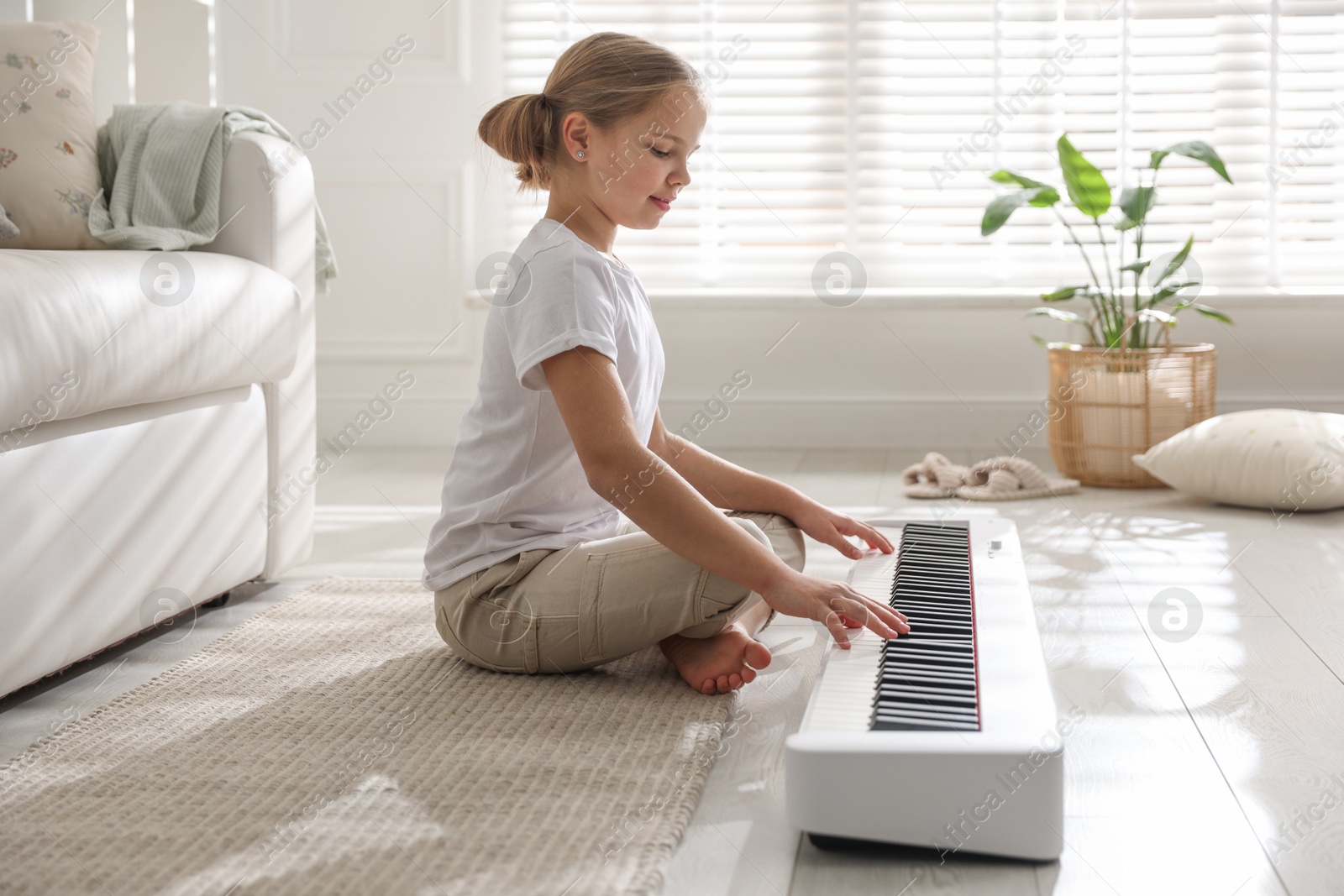 Photo of Cute girl playing synthesizer on floor at home