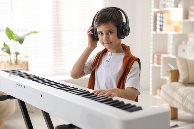 Photo of Cute boy in headphones playing synthesizer at home