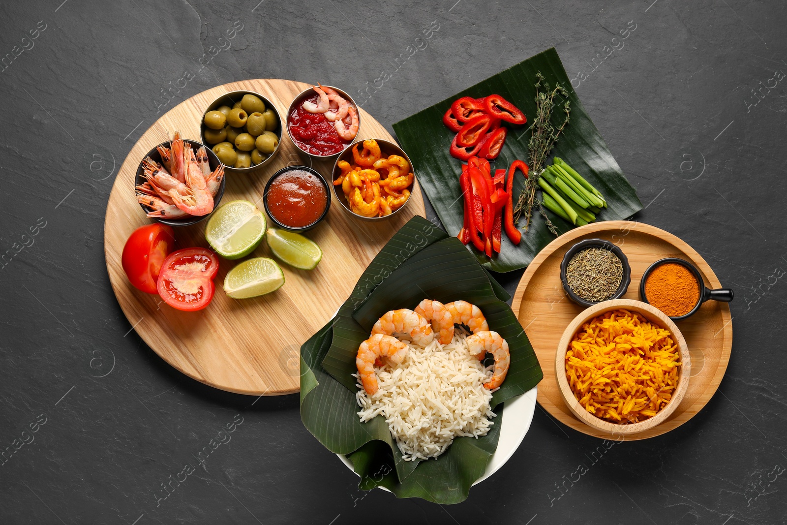 Photo of Cut banana leaves with different food, spices and sauce on dark textured table, flat lay. Healthy eco serving