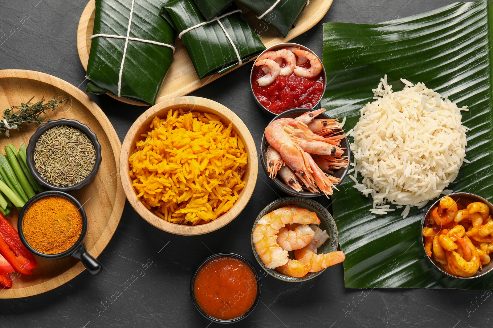 Photo of Cut banana leaves with different food, spices and sauce on dark textured table, flat lay. Healthy eco serving