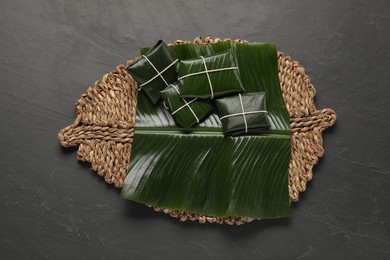 Photo of Different food wrapped in banana leaves on dark table, top view. Healthy eco serving