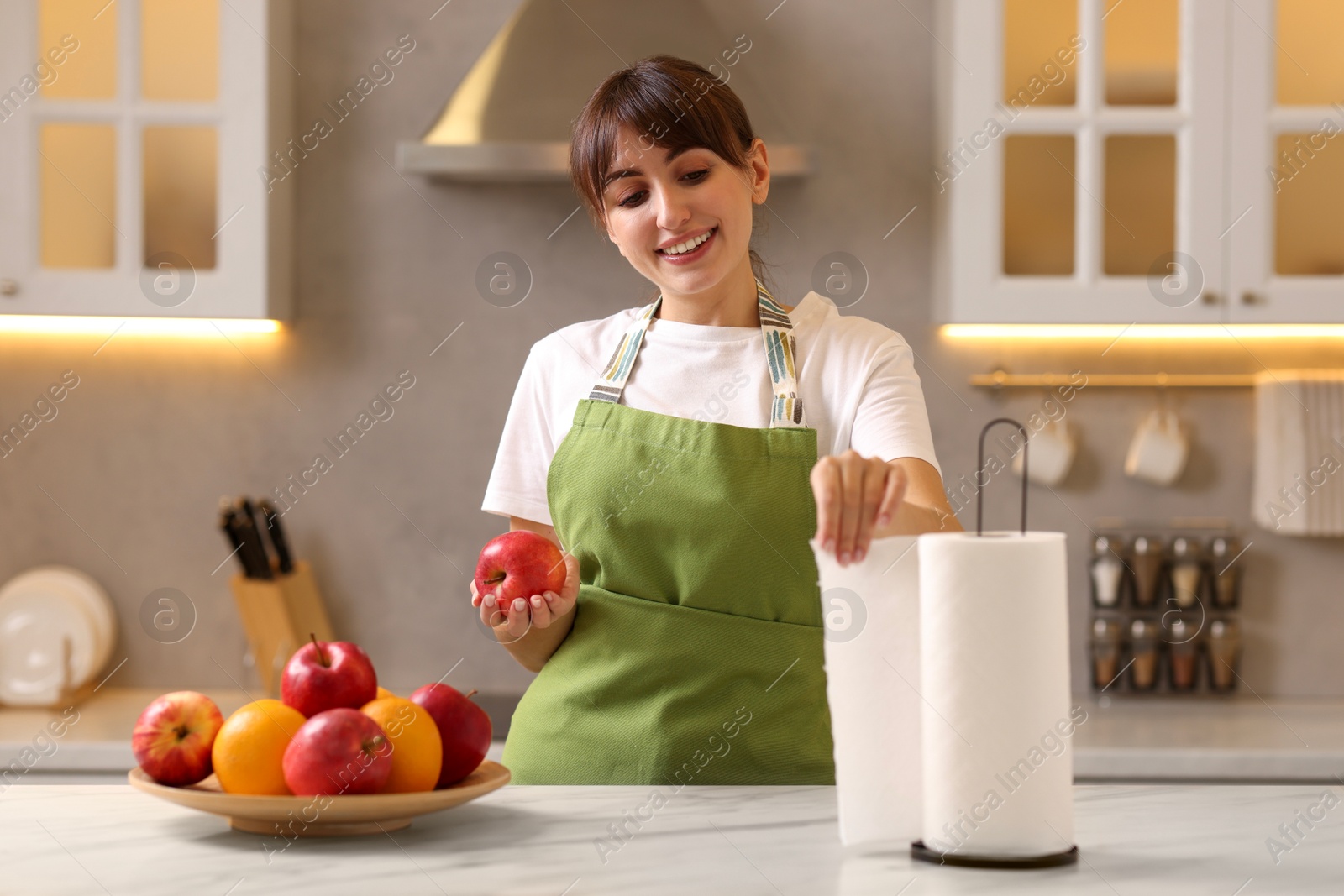 Photo of Woman with apple using paper towels at white marble in kitchen