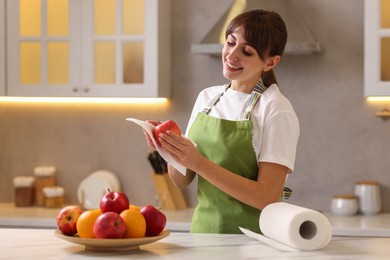 Photo of Woman wiping apple with paper towel at white marble table in kitchen