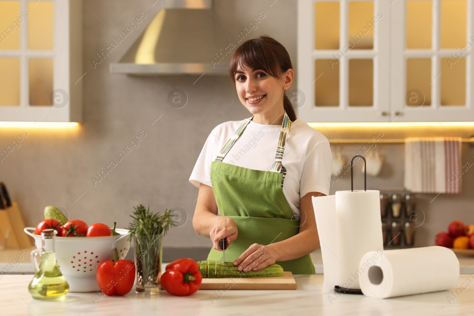 Photo of Woman cutting zucchini at white marble table with rolls of paper towels in kitchen