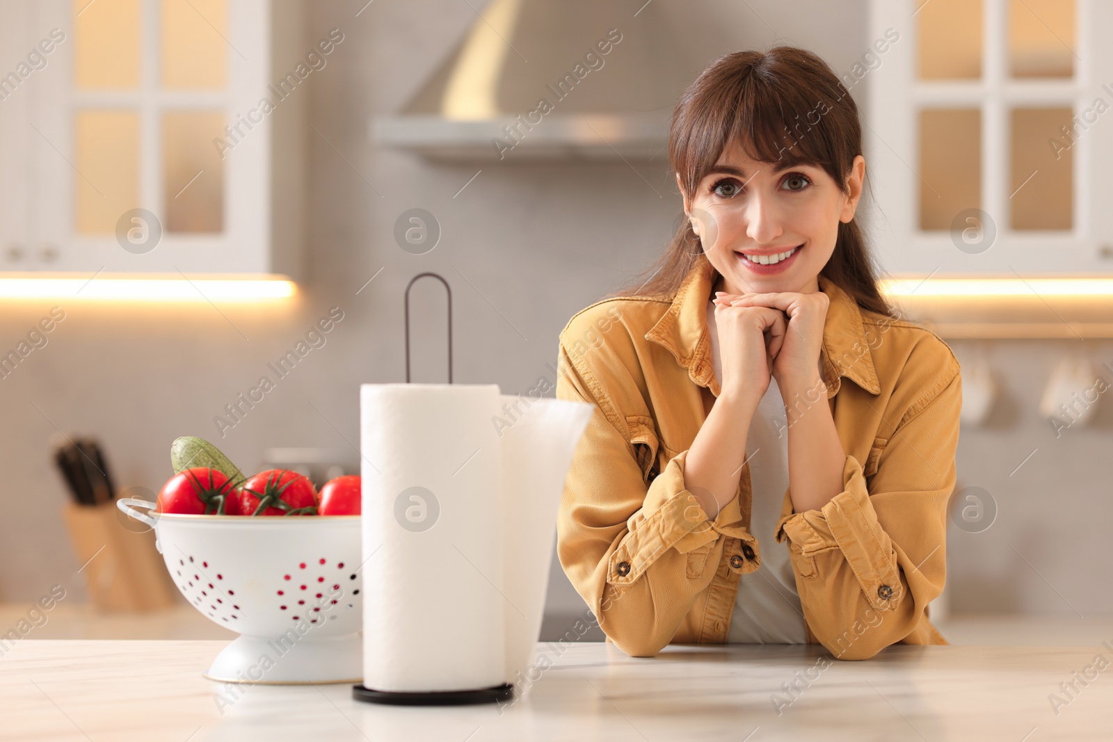 Photo of Woman at white marble table with roll of towels and vegetables in kitchen