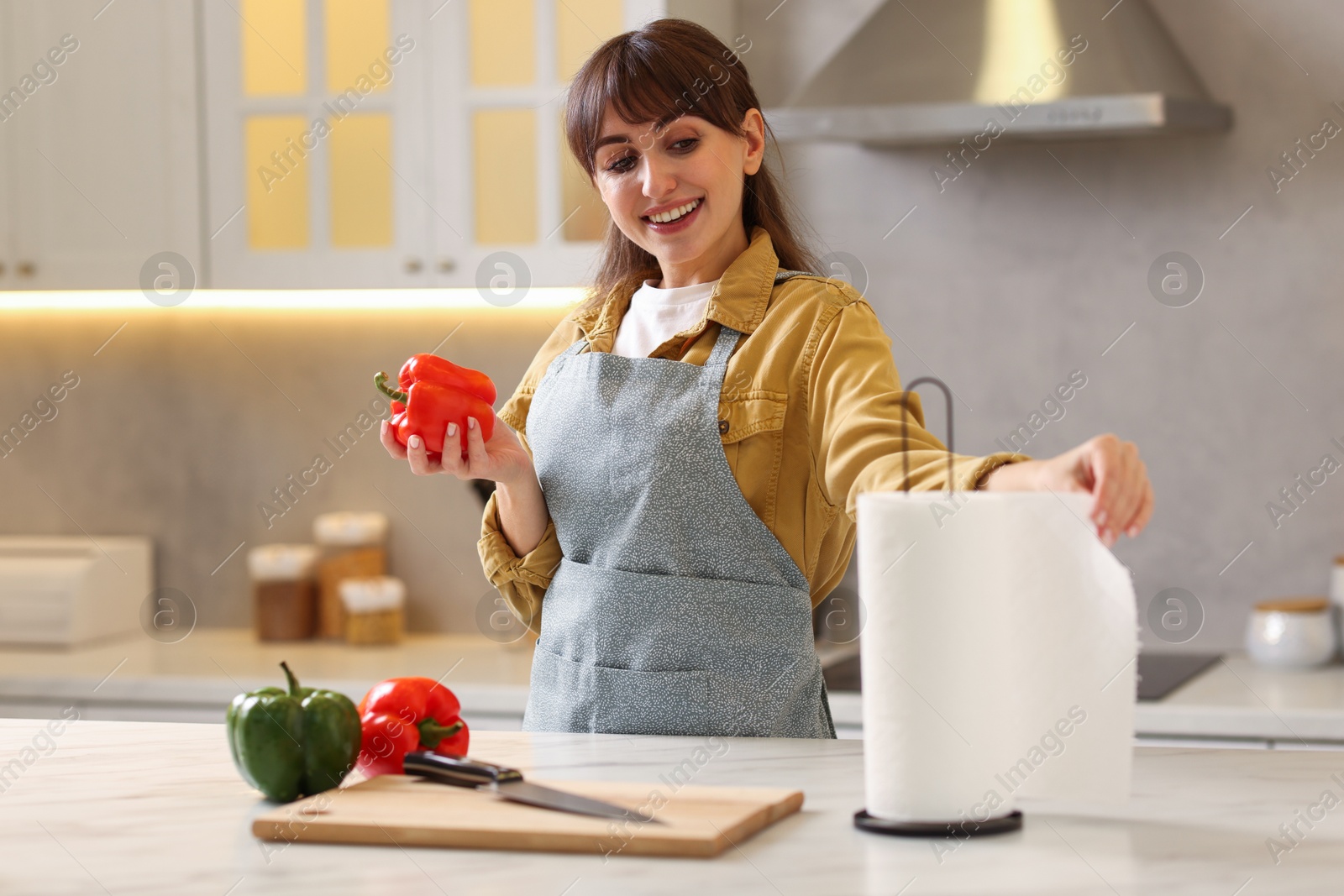 Photo of Woman with bell pepper using paper towels at white marble table in kitchen