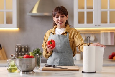 Photo of Woman with bell pepper using paper towels at white marble table in kitchen