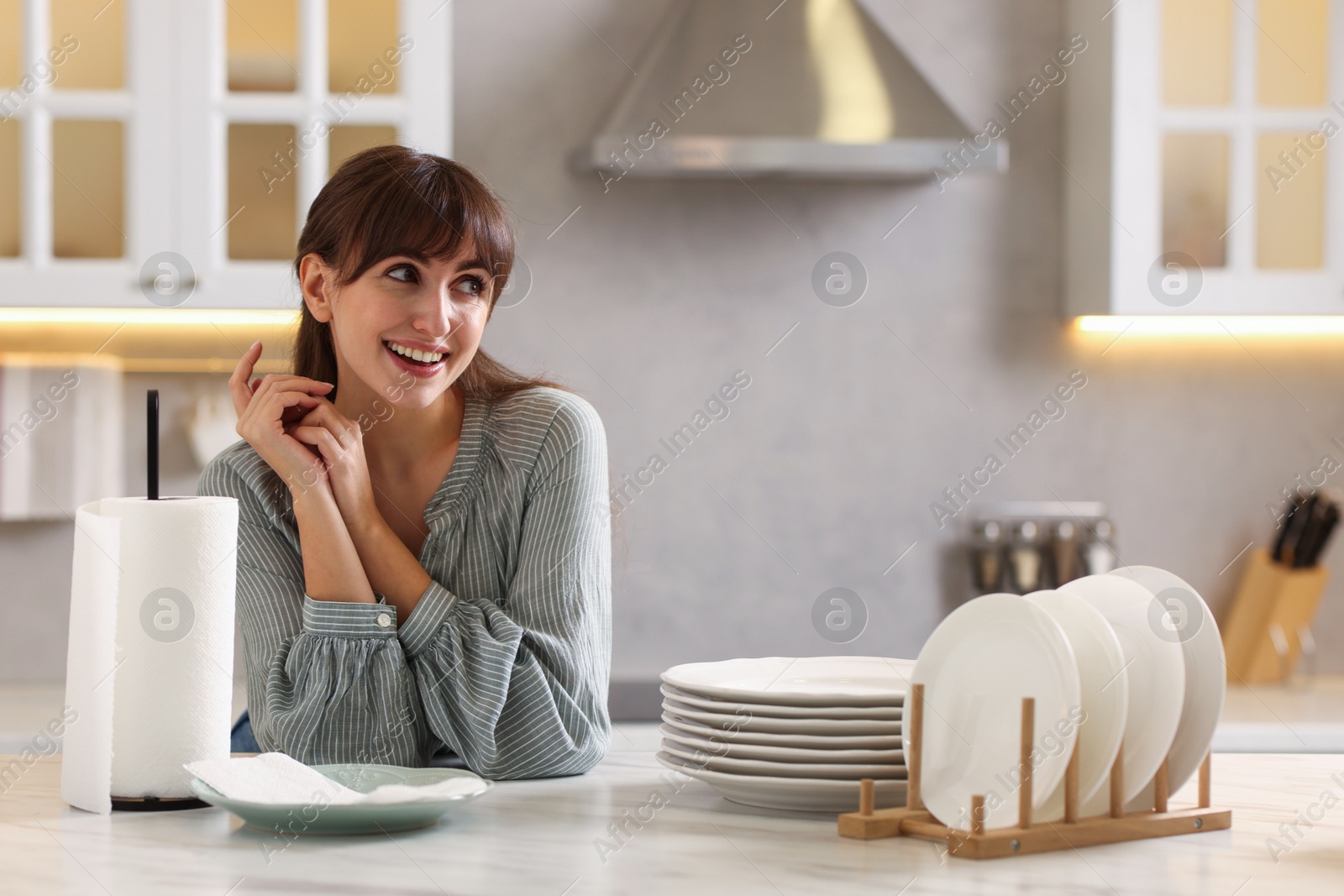 Photo of Woman at white marble table with roll of towels and clean plates in kitchen