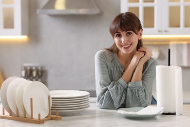 Photo of Woman at white marble table with roll of towels and clean plates in kitchen