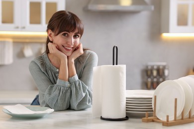 Photo of Woman at white marble table with roll of towels and clean plates in kitchen