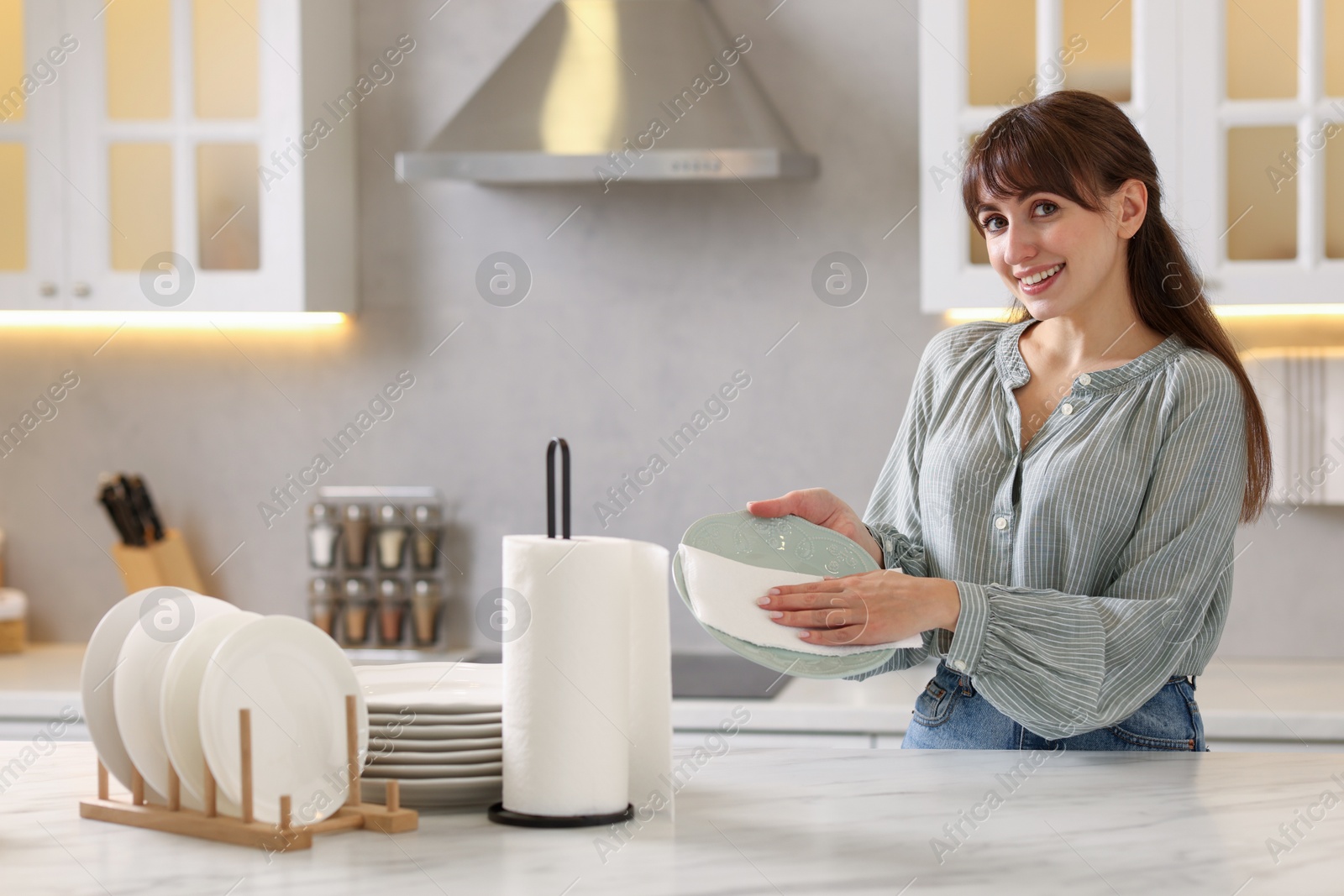 Photo of Woman wiping plate with paper towel at white marble table in kitchen