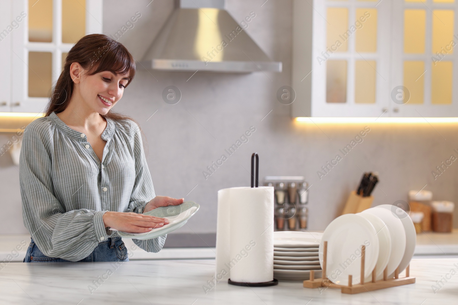 Photo of Woman wiping plate with paper towel at white marble table in kitchen