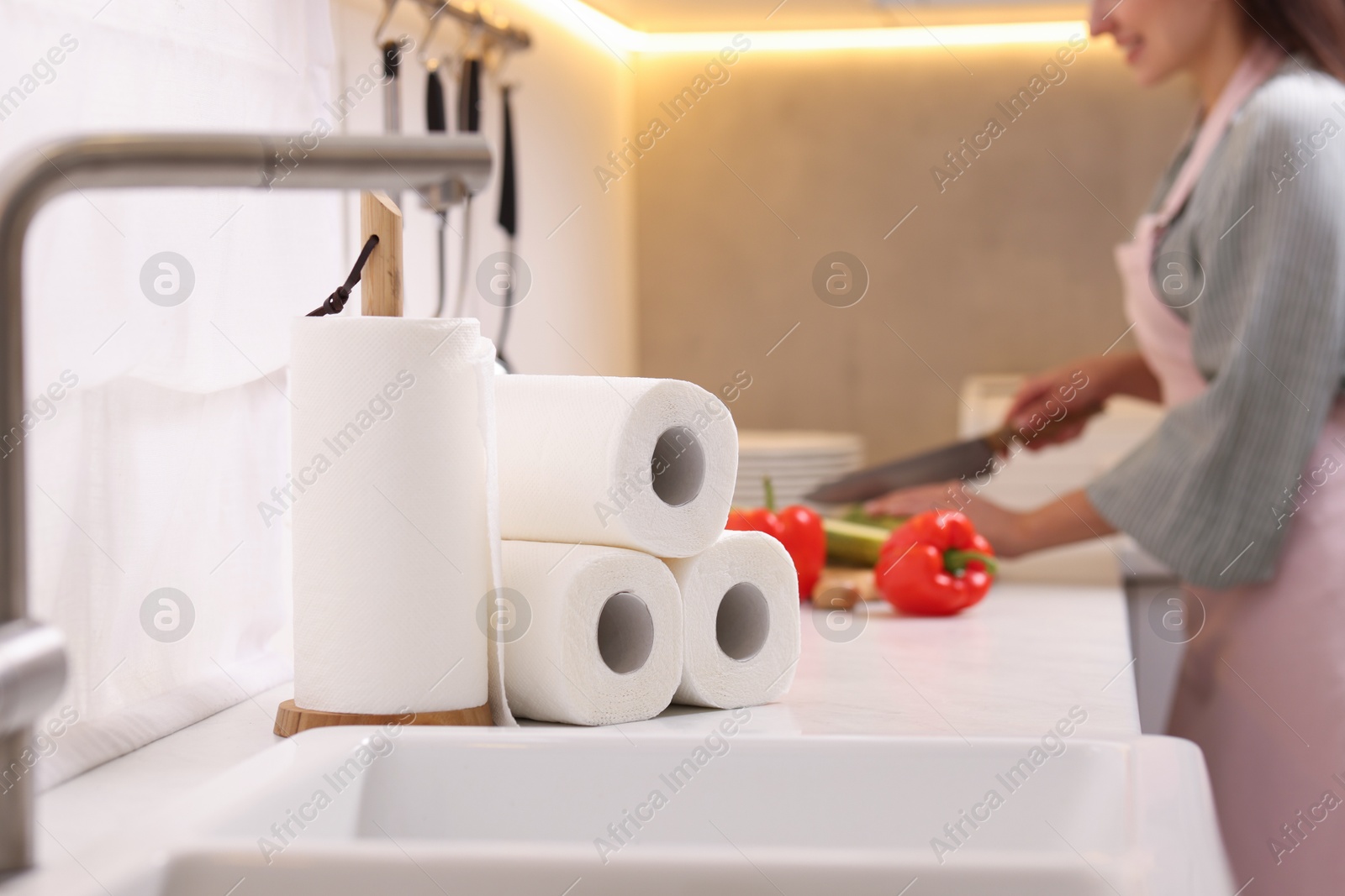 Photo of Woman cutting vegetables at white countertop in kitchen, focus on rolls of paper towels