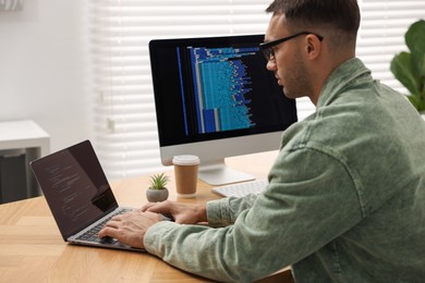 Programmer working on laptop at wooden desk indoors