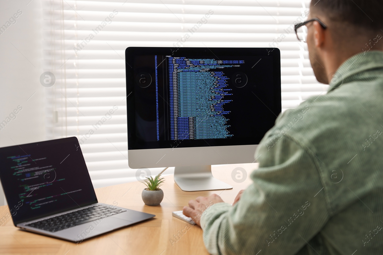 Photo of Programmer working on laptop and computer at wooden desk indoors