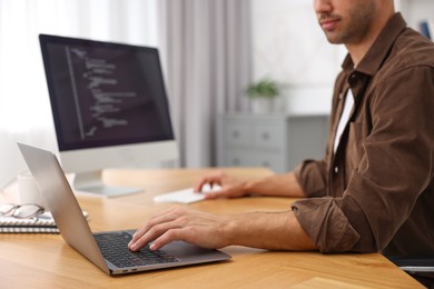 Photo of Programmer working on laptop and computer at wooden desk indoors, closeup