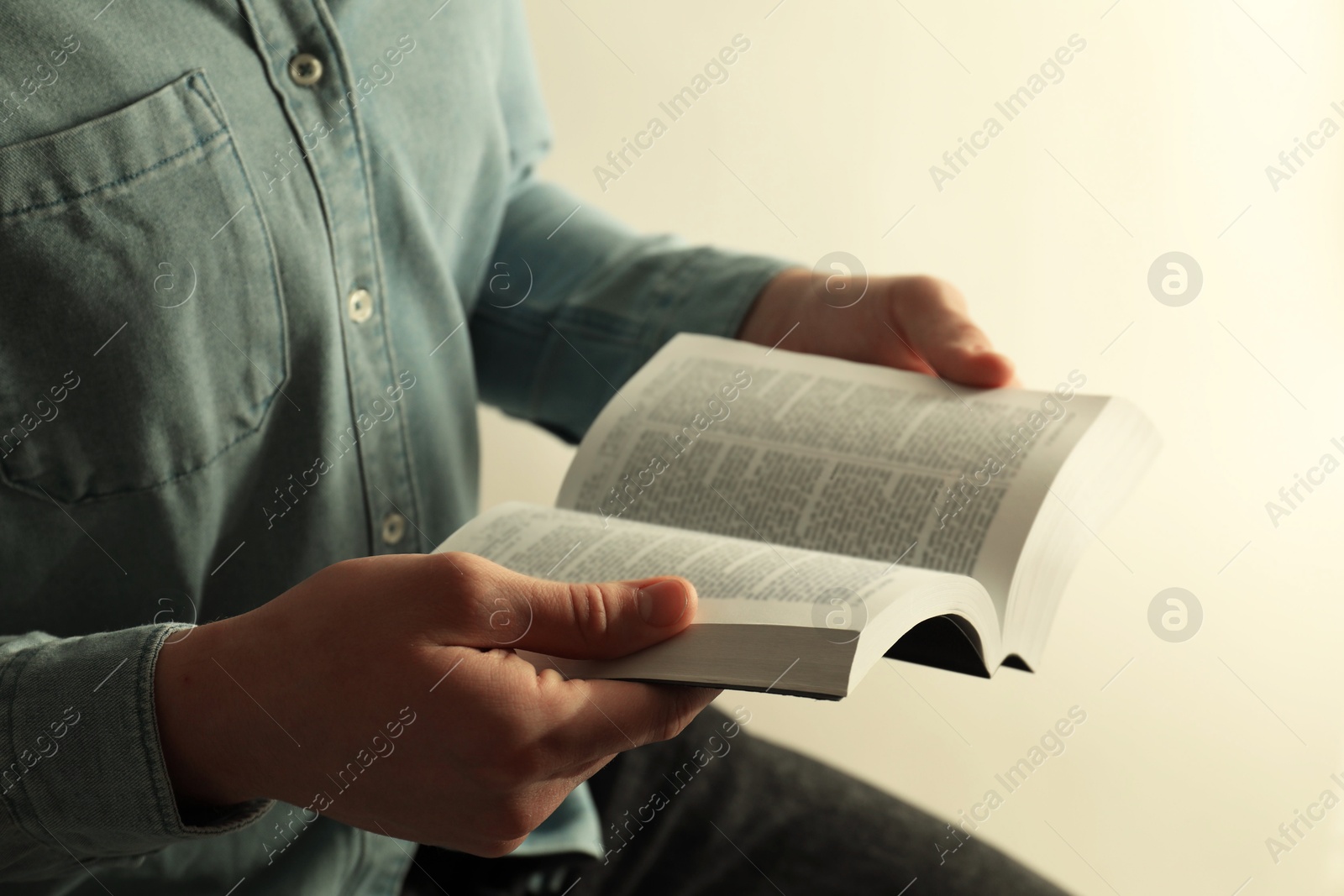 Photo of Man reading Holy Bible on light background, closeup