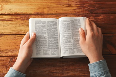 Photo of Man reading Holy Bible in English language at wooden table, top view