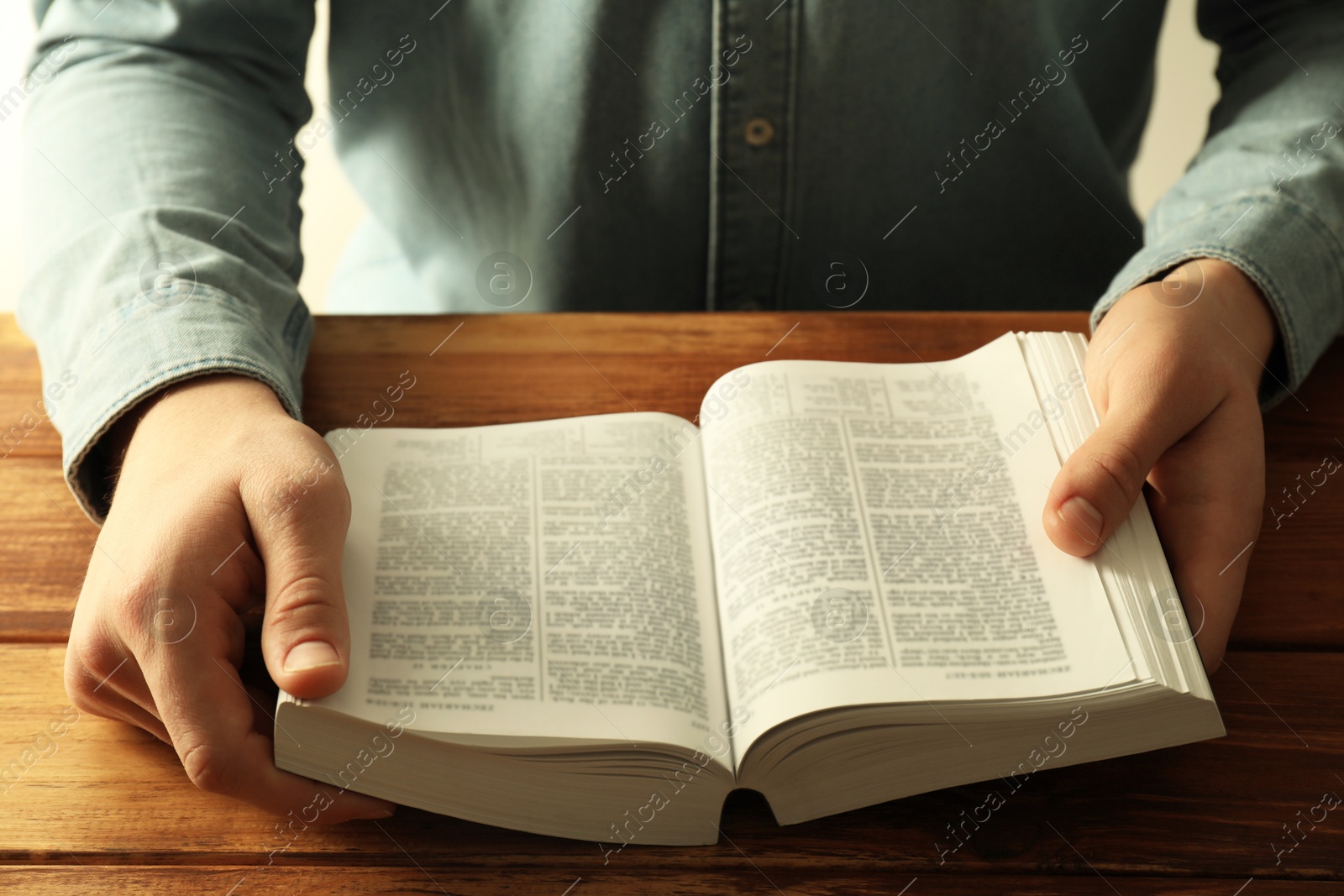 Photo of Man reading Holy Bible in English language at wooden table, closeup