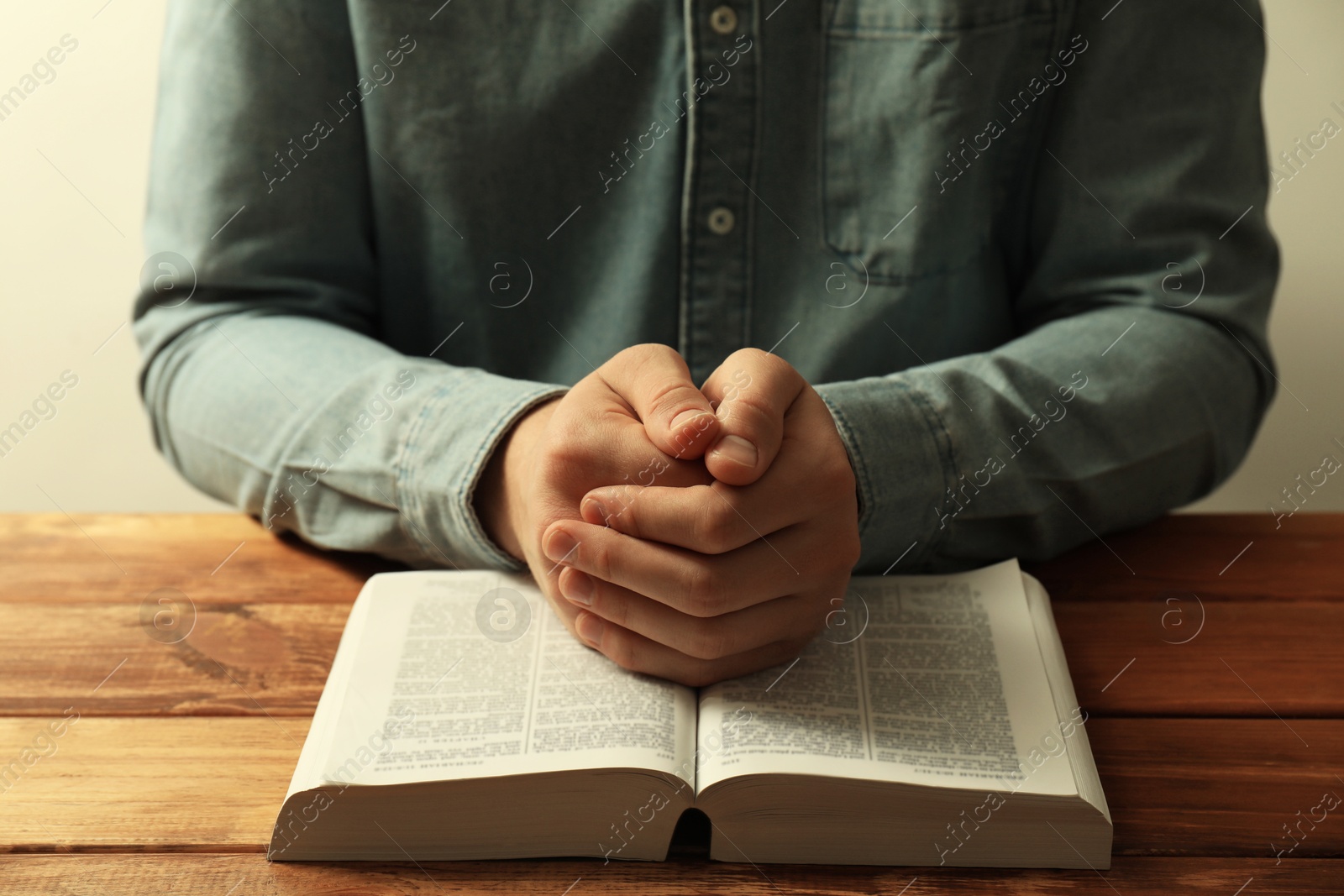 Photo of Man with open Holy Bible praying at wooden table, closeup