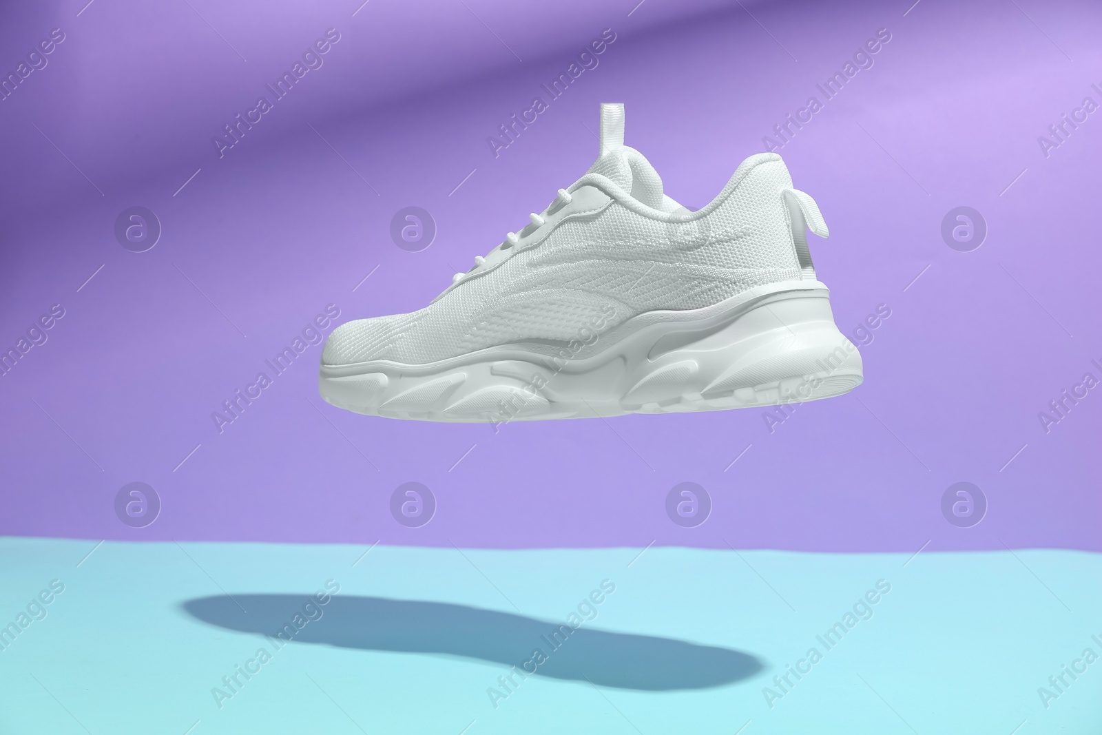 Photo of Stylish white sneaker in air against color background