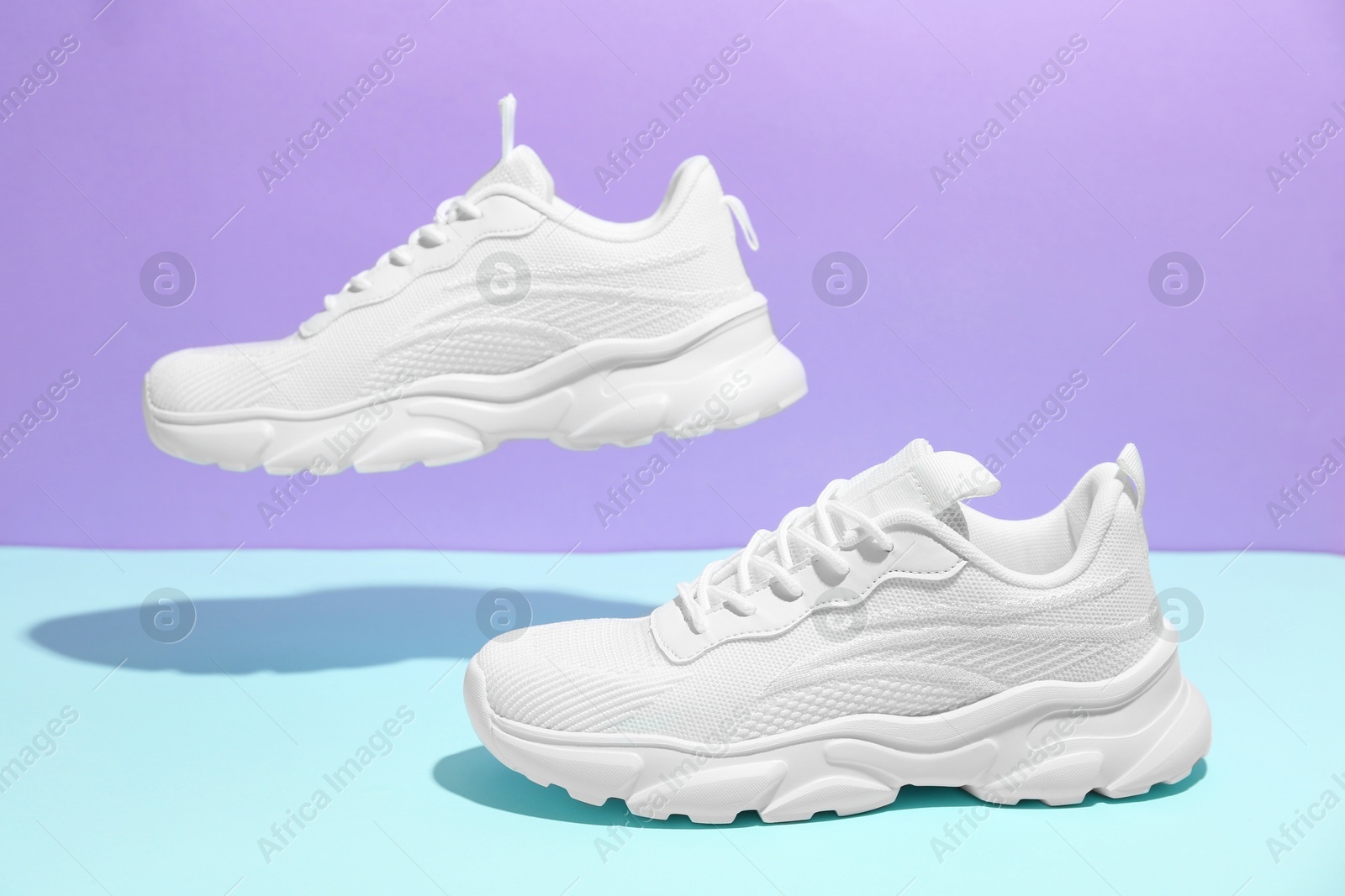 Photo of Pair of stylish white sneakers in air against color background