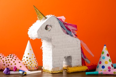 Photo of Bright pinata in shape of unicorn and party accessories on table against orange background