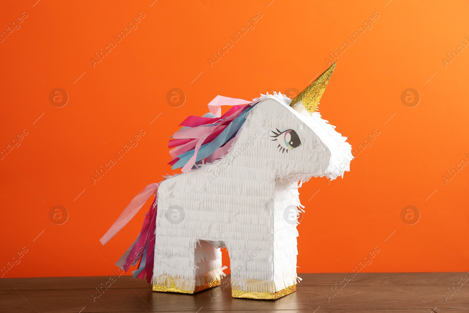 Photo of Bright pinata in shape of unicorn on table against orange background