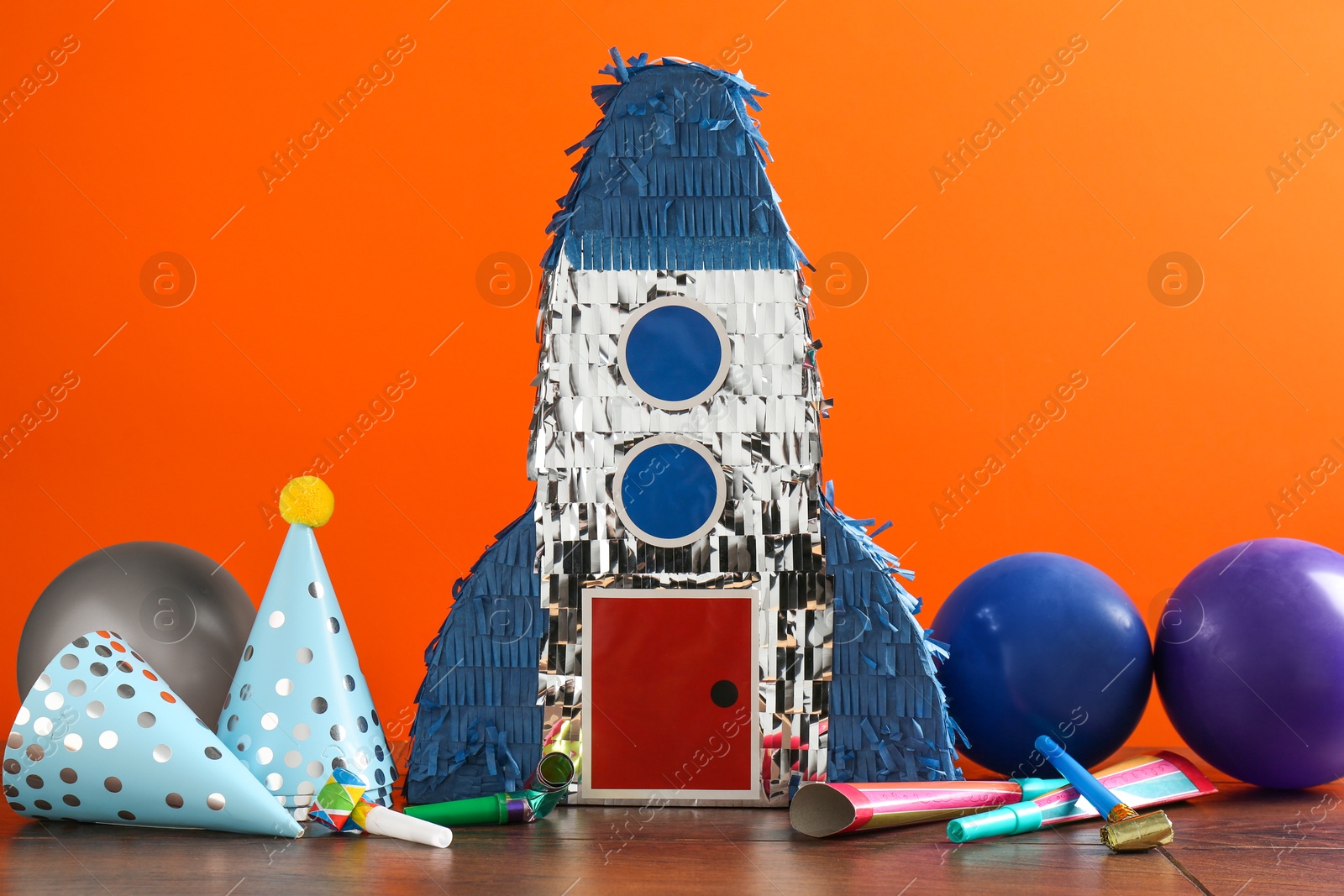 Photo of Bright pinata in shape of spaceship and party accessories on table against orange background